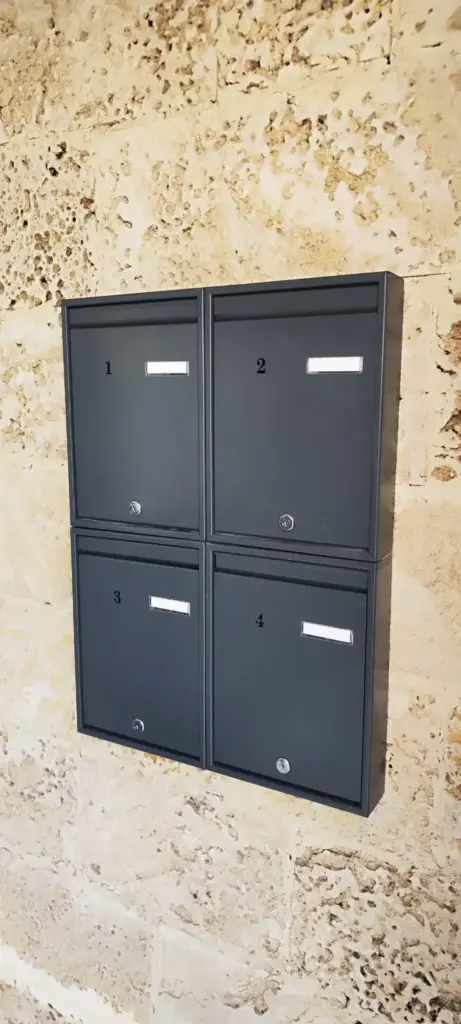 תיבות דואר מעוצבות לבית פרטי, מותקנות על קיר אבן, עם מספרים לכל תיבה.