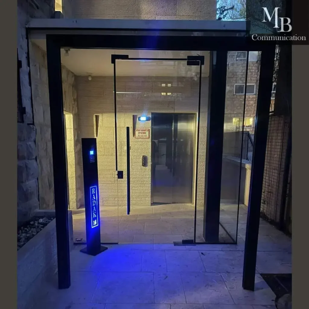 כניסת בניין עם אינטרקום אלחוטי ותאורת לילה, משולבת עם תיבות דואר מעוצבות לבית פרטי.